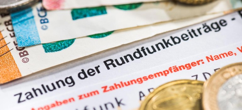 Ein Antrag auf Befreiung vom Rundfunkbeitrag liegt unter ein paar Geldscheinen