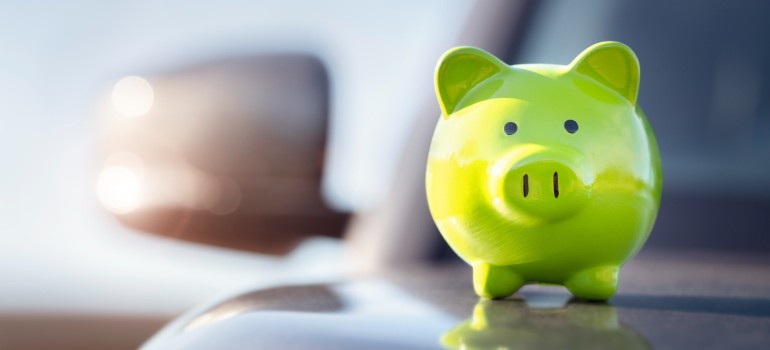 Grünes Sparschwein steht auf der Motorhaube eines Autos