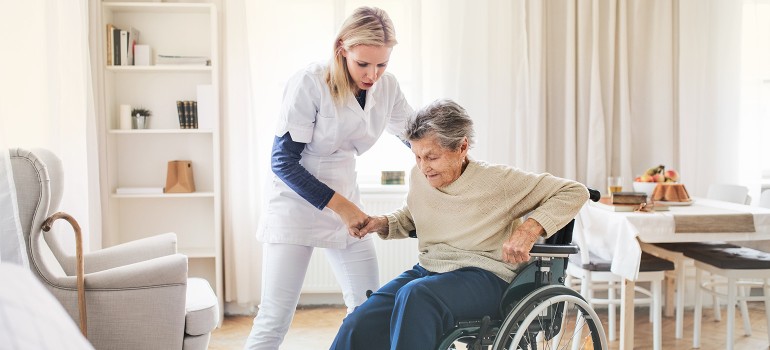 Pflegerin hilft einer alten Dame beim Aufstehen