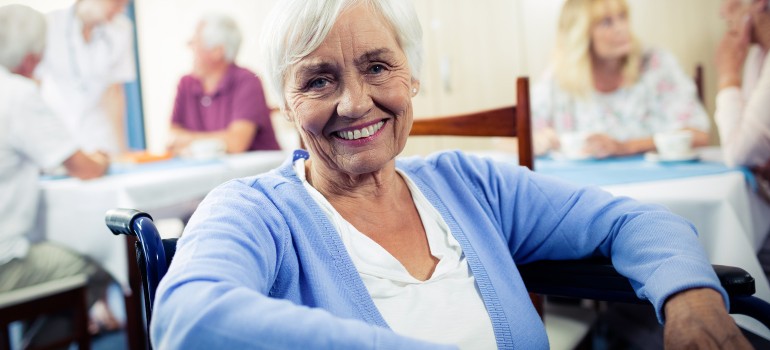 Eine ältere Dame sitzt lächelnd in einem Pflegeheim