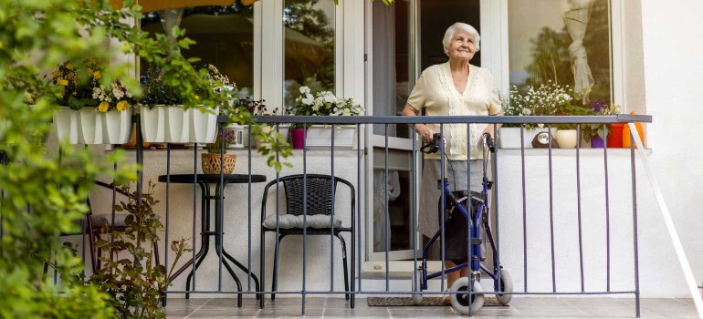 Eine ältere Dame mit Rollator steht lächelnd auf ihrem Balkon