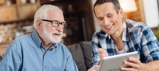 Angehöriger zeigt älterem Mann Beschäftigungsideen bei Demenz auf einem Tablet