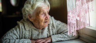 Ältere frau schaut aus dem Fenster. Interview zurm Thema Altersdepression.