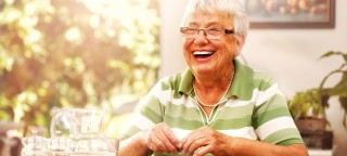 Appetit trotz Schluckstörungen: Ältere Dame sitzt am Tisch und lächelt