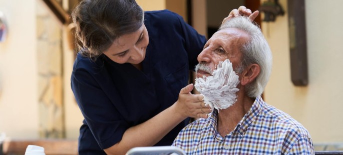 Ein älterer Mann wird von einer Frau rasiert